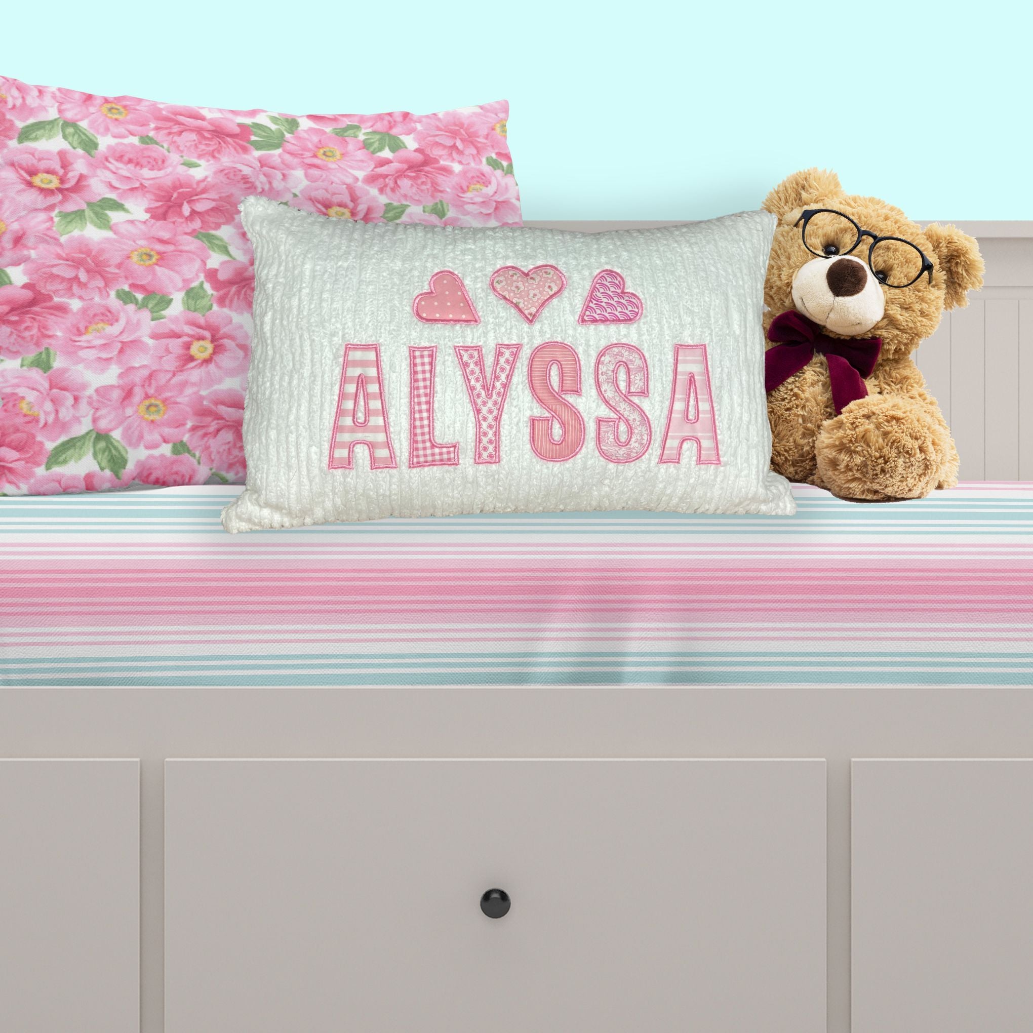 name pillow for girls with white chenille background and pink applique name and hearts - shown on bed