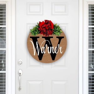 personalized stained wood wreath with family name and initial. red and black plaid with red bow and greenery. 18 inches round solid wood