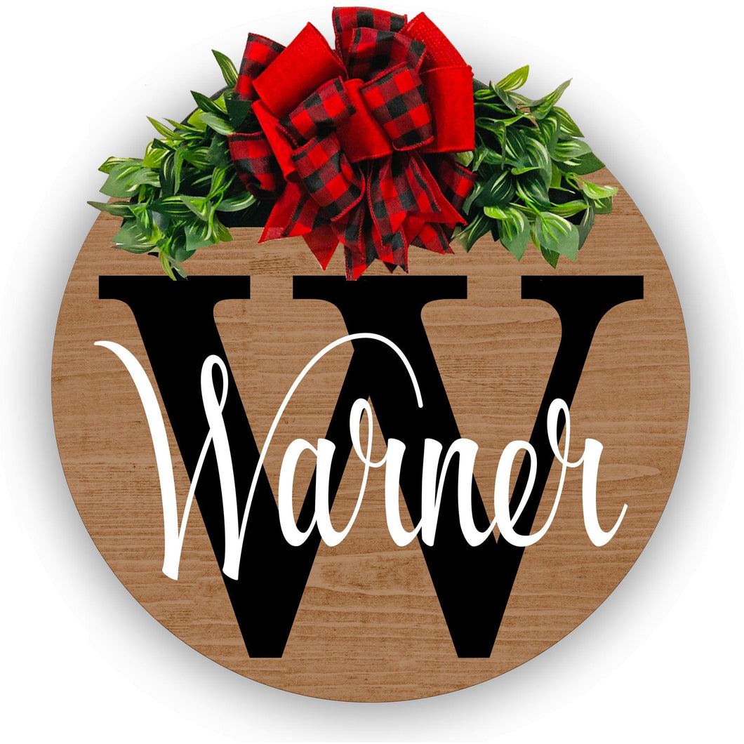 personalized stained wood wreath with family name and initial. red and black plaid with red bow and greenery. 18 inches round solid wood
