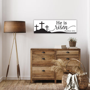 painted wood sign measures 7.25 by 23.5 inches. three crosses on a hill with He is risen text and Matthew 28:6. white background with black design.