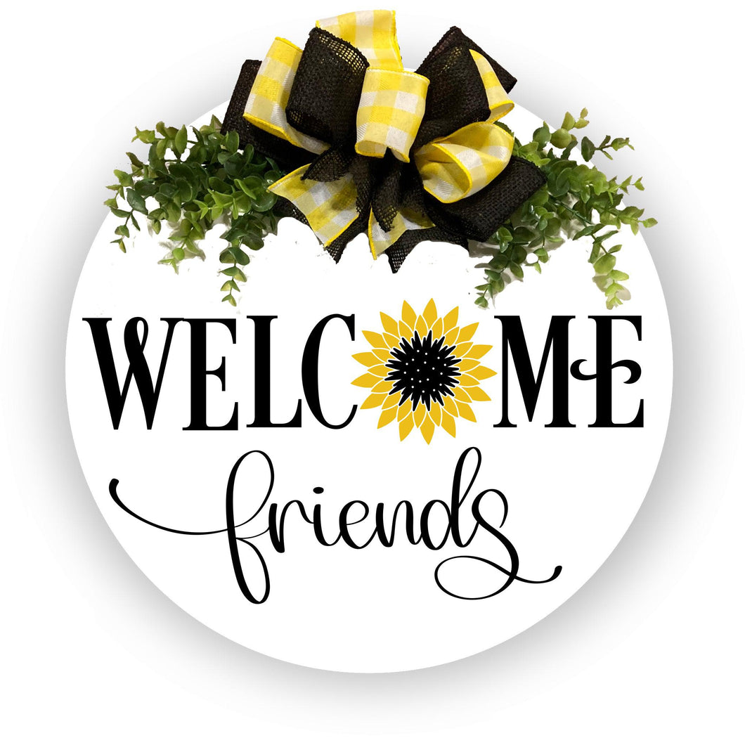 White painted 18 inch wood round door hanger.  welcome friends text with yellow and black sunflower. yellow and white plaid and black bow with greenery