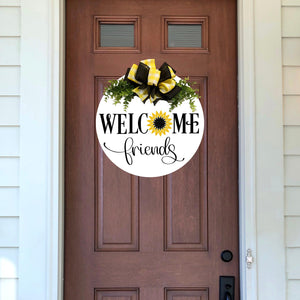 White painted 18 inch wood round door hanger. welcome friends text with yellow and black sunflower. yellow and white plaid and black bow with greenery